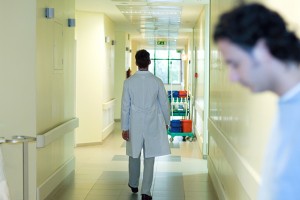 Male doctor walking in hospital corridor, full length, rear view, man in foreground